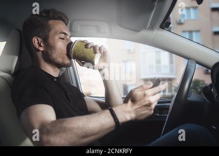 Un homme assis dans la voiture tient le café et le téléphone Banque D'Images