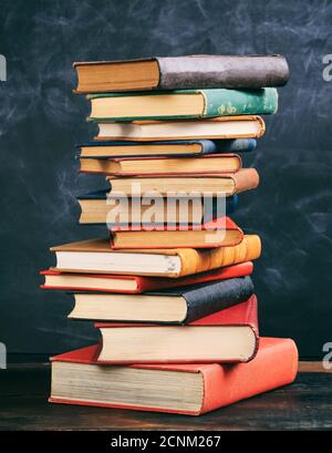 Livres empilés sur un bureau en bois, fond de tableau noir. Vieux livres de couverture rigide vintage, école, éducation, concept de la science. Banque D'Images