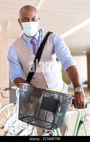 Homme d'affaires noir qui garait son vélo. Il porte un masque médical et un vêtement formel. Concept de vie saine et nouvelle normale. Banque D'Images