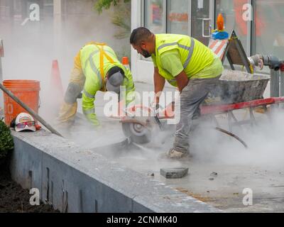 Travailleur avec une scie circulaire refroidie à l'eau coupant des blocs de chaussée en pierre. Projet de reconstruction de la rue Lake. Oak Park, Illinois. Banque D'Images