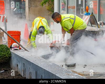 Travailleur avec une scie circulaire refroidie à l'eau coupant des blocs de chaussée en pierre. Projet de reconstruction de la rue Lake. Oak Park, Illinois. Banque D'Images