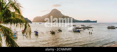 Scène panoramique du voyage les bateaux de tourisme reviennent à El Nido à la lumière du coucher du soleil. Palawan, Philippines. Île de Cadlao en arrière-plan. Banque D'Images