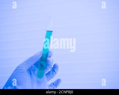 Main d'un scientifique dans un gant tenant un tube à essai en verre avec un liquide bleu à l'intérieur, tons de couleur. Gros plan Banque D'Images
