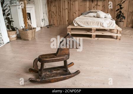 Chambre à l'intérieur en bois avec un cheval en bois. Il y a un cheval pour enfants au premier plan. En arrière-plan se trouve un lit et une cheminée. Élevée Banque D'Images