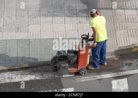 Ouvrier de construction coupant des sols en béton avec une machine à lame de scie diamantée sur un trottoir Banque D'Images