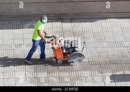 Ouvrier de la construction coupant le plancher de pierre de pavage avec la lame de scie au diamant machine sur un trottoir Banque D'Images