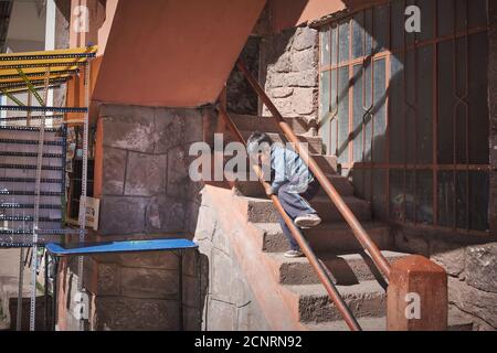 Un jeune enfant joue sur les mains courantes de quelques marches escaliers dans le village principal de l'île Taquile, lac Titicaca, Pérou Banque D'Images