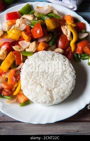 Le riz bouilli avec le poulet et les légumes saute dans un assiette blanche avec ingrédients sur fond Banque D'Images