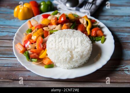 Gros plan du riz bouilli avec le poulet et les légumes faites revenir dans une assiette blanche avec des ingrédients sur un fond Banque D'Images