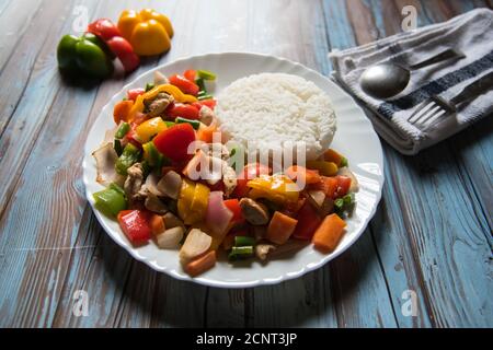 Le riz ainsi que le poulet et les légumes saute dans un blanc assiette avec ingrédients sur fond Banque D'Images