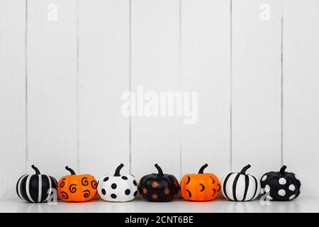 Citrouilles d'Halloween à motifs noir, blanc et orange en rangée sur fond de bois blanc. Copier l'espace. Banque D'Images