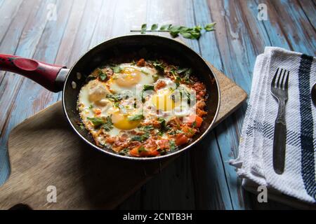 Shakshuka, une spécialité du Moyen-Orient, préparée avec des œufs, des oignons, des tomates dans une casserole noire sur fond Banque D'Images