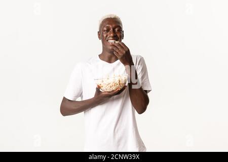 Portrait d'un jeune homme afro-américain joyeux et séduisant qui apprécie le film et les repas de pop-corn, regardant la télévision sur fond blanc Banque D'Images