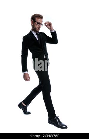 un jeune homme d'affaires sérieux qui marche à la mode, regarde à côté, frognant et fixant des lunettes sur fond blanc Banque D'Images