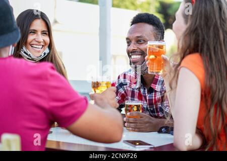 Des amis multiraciaux applaudissent avec de la bière et sourient en riant avec chacun Autres - personnes multiethniques avec masque de visage ayant le plaisir dehors Banque D'Images