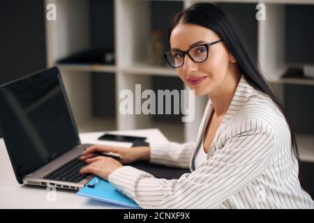 Concentrés belle jeune businesswoman working on laptop in bright modern office Banque D'Images