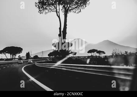 Photo artistique en noir et blanc d'une autoroute en Italie avec silhouette de cèdre, voitures de conduite et vulcano Vésuve en arrière-plan. Banque D'Images