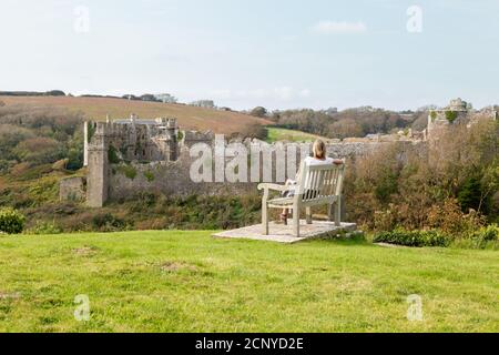 Vue sur le château de Manorbier avec une femme assise sur un banc, Pembrokeshire, pays de Galles, Royaume-Uni Banque D'Images