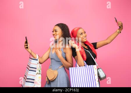 deux belles femmes africaines avec des sacs de shopping prenant des selfies debout retour à l'arrière Banque D'Images