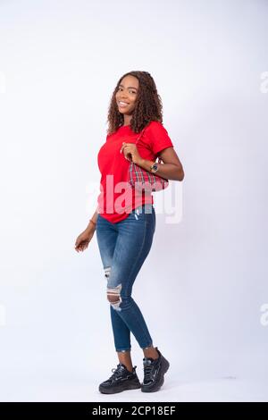 portrait d'une jeune femme noire confiante se posant devant un fond blanc, portant un sac à main Banque D'Images