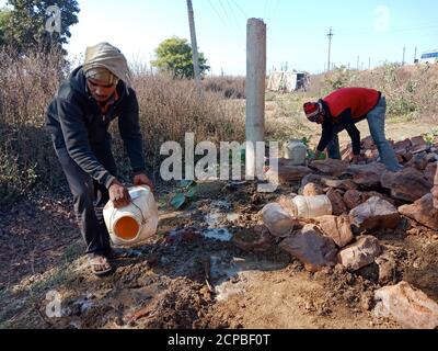 DISTRICT KATNI, INDE - 13 DÉCEMBRE 2019 : une main-d'œuvre indienne qui répand de l'eau sur le chantier de construction. Banque D'Images