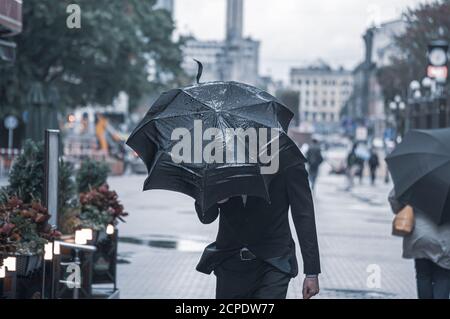 Un homme d'affaires en costume abrite un parapluie de la pluie et du vent dehors par mauvais temps. Banque D'Images