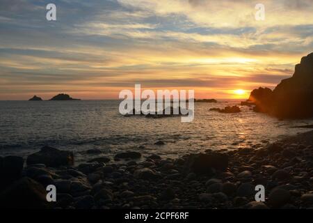 Le soleil se couche depuis le cap Cornwall à Cornwall, au Royaume-Uni, avec une plage en premier plan et les Brisons rochers à l'horizon Banque D'Images