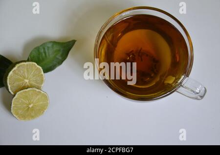 Tasse et théière transparentes avec thé noir, préparation de thé sec sur la table, tranches de bergamote ou citron ou lime sur fond blanc Banque D'Images