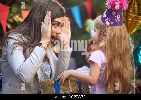 belle brunette caucasienne jouant peek un boo avec mignon petit fille blonde à la fête d'anniversaire Banque D'Images