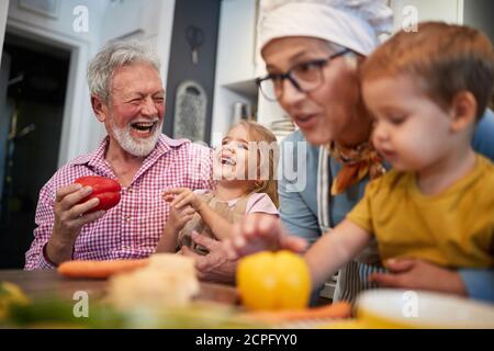 Les grands-parents caucasiens s'amusent avec leurs petits-enfants dans la cuisine jouer avec les légumes Banque D'Images