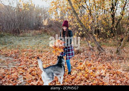 Jeune femme heureuse jouant avec son chien dans le parc d'automne. Husky sautant pour les feuilles d'automne Banque D'Images