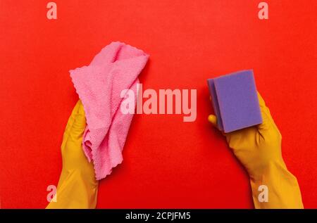 Mains en caoutchouc gants jaunes tenir un chiffon rose et une éponge pourpre sur un fond jaune. Place pour le texte. Banque D'Images