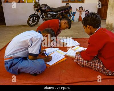 DISTRICT KATNI, INDE - 13 JANVIER 2020 : une fille indienne de l'école primaire écrit sur le livre à fond ouvert portant l'uniforme de couleur rouge. Banque D'Images