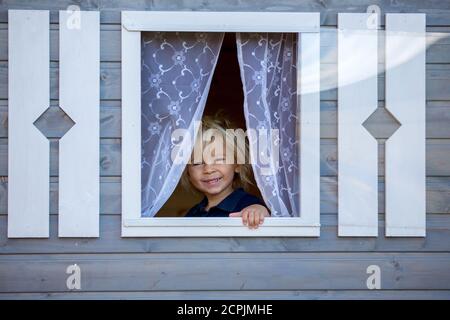 Adorable petit garçon, jouant dans une maison de poupée en bois dans le jardin, regardant dehors Banque D'Images