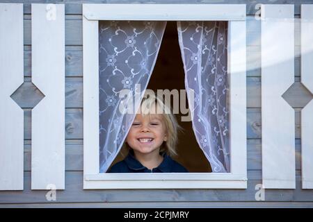 Adorable petit garçon, jouant dans une maison de poupée en bois dans le jardin, regardant dehors Banque D'Images