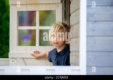 Adorable petit garçon, jouant dans une maison de poupée en bois dans le jardin, regardant dehors Banque D'Images