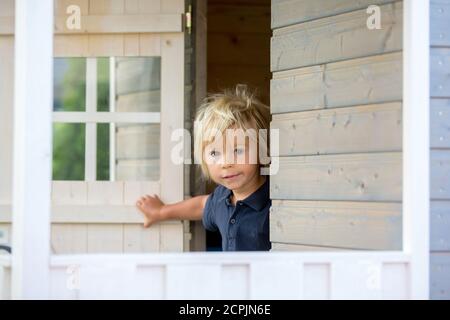 Adorable petit garçon, jouant dans une maison de poupée en bois dans le jardin, regardant dehors Banque D'Images