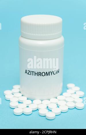 AZITROMYCIN antibiotique dans un emballage en flacon blanc avec des comprimés épars. Traitements pour COVID-19. Isolé sur fond bleu. Gros plan. Tir vertical. Banque D'Images