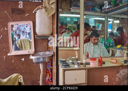 Les miroirs d'un salon de coiffure à Mumbai, en Inde, reflètent le coiffeur et le client plusieurs fois, tandis qu'un autre miroir reflète la vie de la rue à l'extérieur Banque D'Images