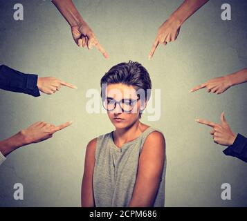 Concept d'accusation coupable timide personne fille. Triste embarrassé bouleversé femme dans les lunettes regardant vers le bas beaucoup de doigts pointant vers son mur isolé gris dos Banque D'Images