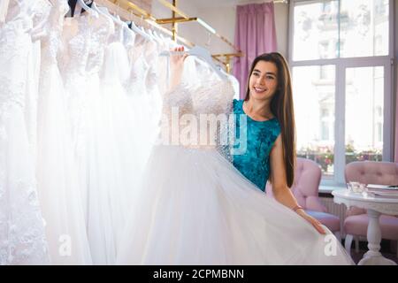 Happy mariée choisit une robe dans une boutique de mariage Banque D'Images