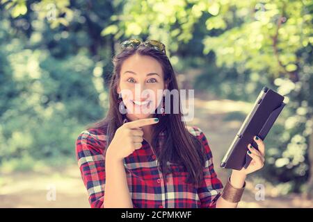 Jeune femme attirante pointant avec le doigt sur son ordinateur de tablette debout à l'extérieur dans le parc le jour ensoleillé d'été Banque D'Images