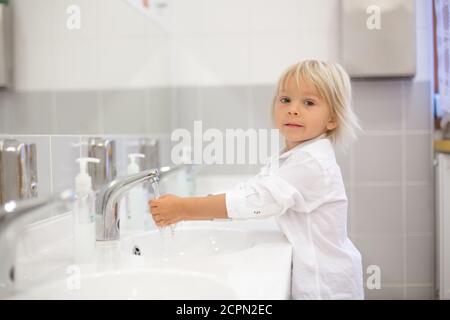 Petit enfant d'âge préscolaire, garçon blond, se laver les mains dans la salle de bains dans un jardin d'enfants, habitudes d'hygiène Banque D'Images