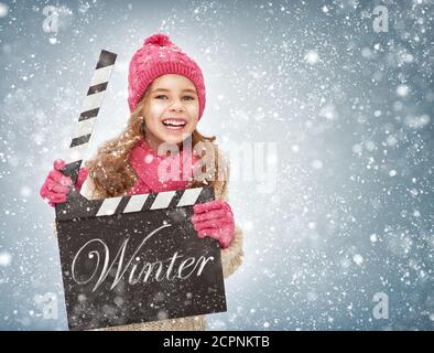 enfant fille dans des vêtements d'hiver tenant la planche de clapper dans les mains. Banque D'Images