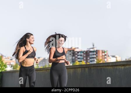 deux jeunes amies vêtu de vêtements de sport noirs et de course à pied sur un parc urbain avec vue sur les bâtiments de la ville l'arrière-plan Banque D'Images