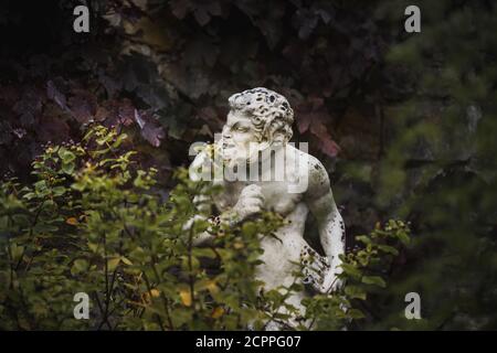 Château de Hever, 30 août 2020 : statue blanche de Pan le dieu grec avec une flûte dans sa main se cachant derrière le feuillage qui a l'air gaie Banque D'Images