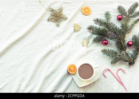 Mise en page du nouvel an avec tasse de café ou de cacao, branches de sapin, décorations de Noël, bonbons en bâtonnets, oranges séchées. Vue de dessus, plat, espace de copie. Banque D'Images