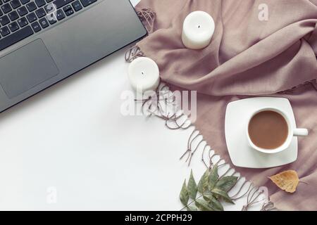 Bureau confortable avec ordinateur portable, châle, bougies et feuilles d'automne. Concept d'automne, espace de copie. Banque D'Images