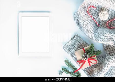 Mise en page de Noël avec ordinateur tablette avec écran vierge, chandail en maille, cadeau dans une boîte, brindilles de sapin, Cannes de bonbons rouges sur fond blanc, vue du dessus, fla Banque D'Images