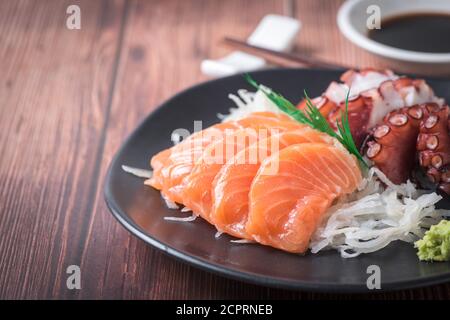 Saumon et tako sashimi sur un plat noir avec baguettes, cuisine japonaise, fond de bois Banque D'Images